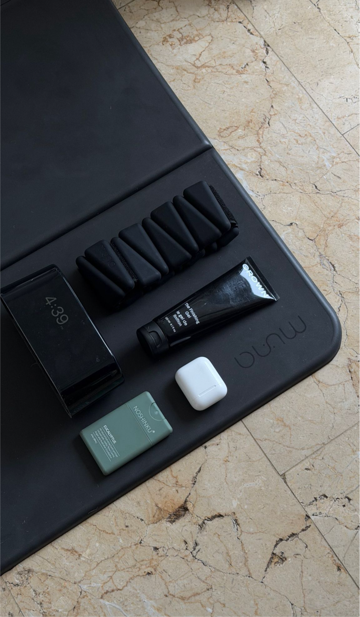 Makeup products including a tube and a compact on a black tray with a marble floor background.