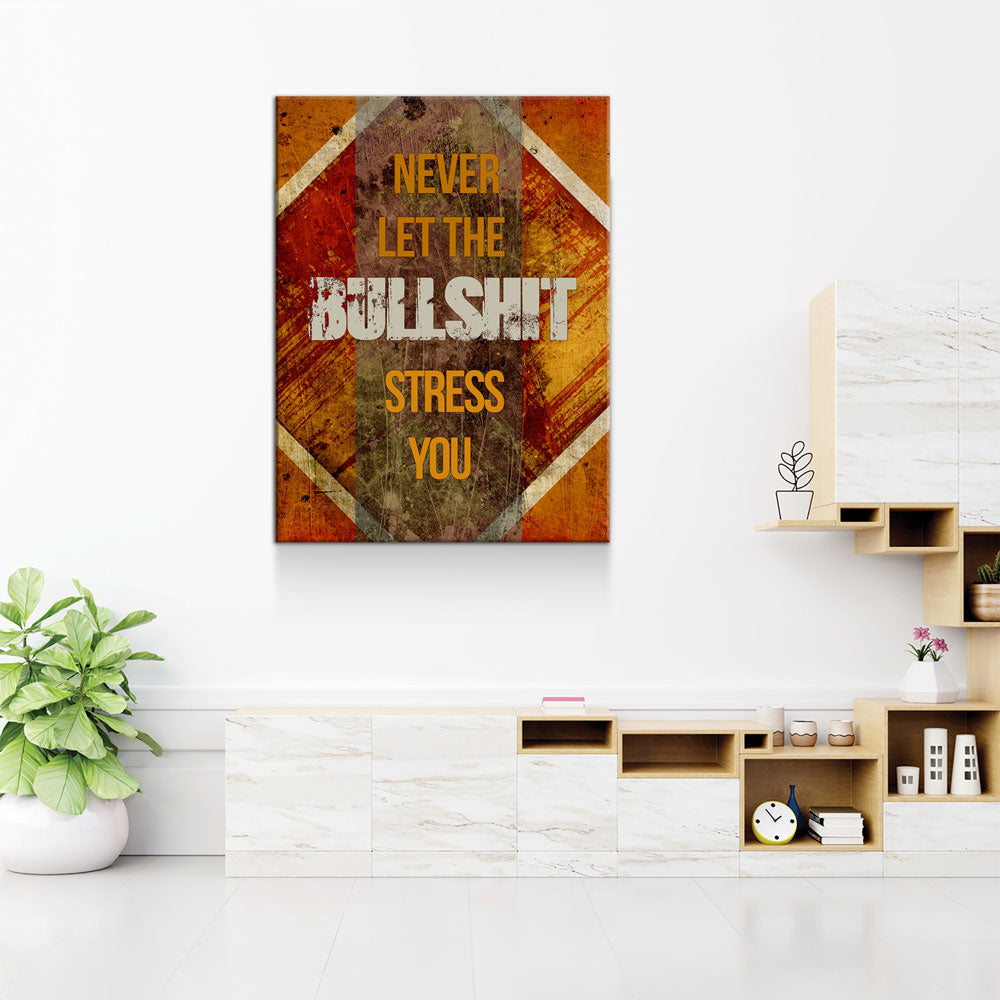 A vertical canvas wall art print with the motivational quote 'NEVER LET THE BULLSHIT STRESS YOU' in yellow and white text over a distressed orange, brown, and gold geometric background. The canvas is displayed on a white wall in a modern, minimalist living room setting with a marble console, wooden shelves, and a potted green plant.