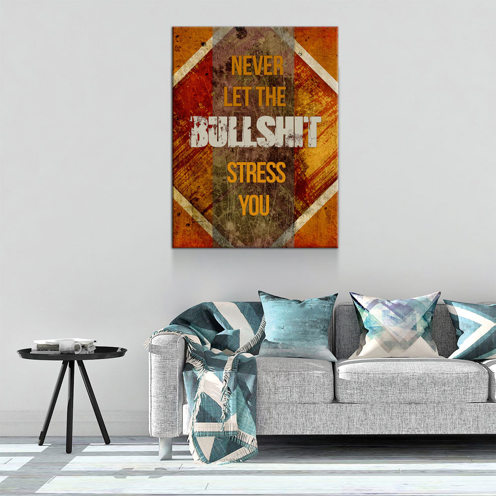 A rectangular wall art print with distressed orange, brown, and cream tones hangs above a gray sofa in a styled living room. The print contains the text 'NEVER LET THE BULL SHIT STRESS YOU' in yellow and white lettering.