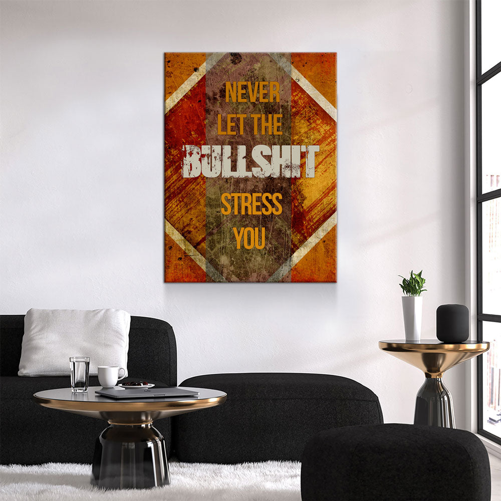 A rectangular wall art print with a distressed orange, brown, and beige graphic background hangs above a black sofa in a modern living room. The print features the text 'NEVER LET THE BULL SHIT STRESS YOU' in yellow and white lettering.