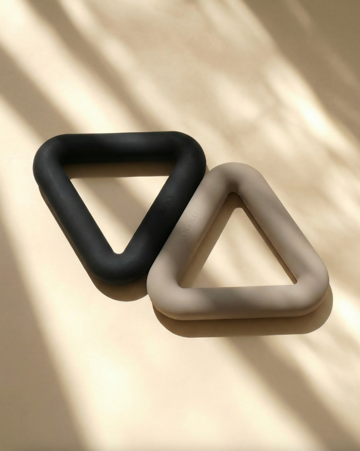Two triangle-shaped rings, one black and one beige, on a beige background with shadows.