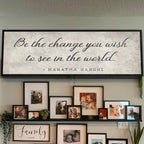 Wall with framed photos and a large Gandhi quote sign