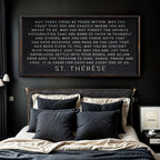 Bedroom with a quote from St. Therese on the wall above a bed with dark pillows.