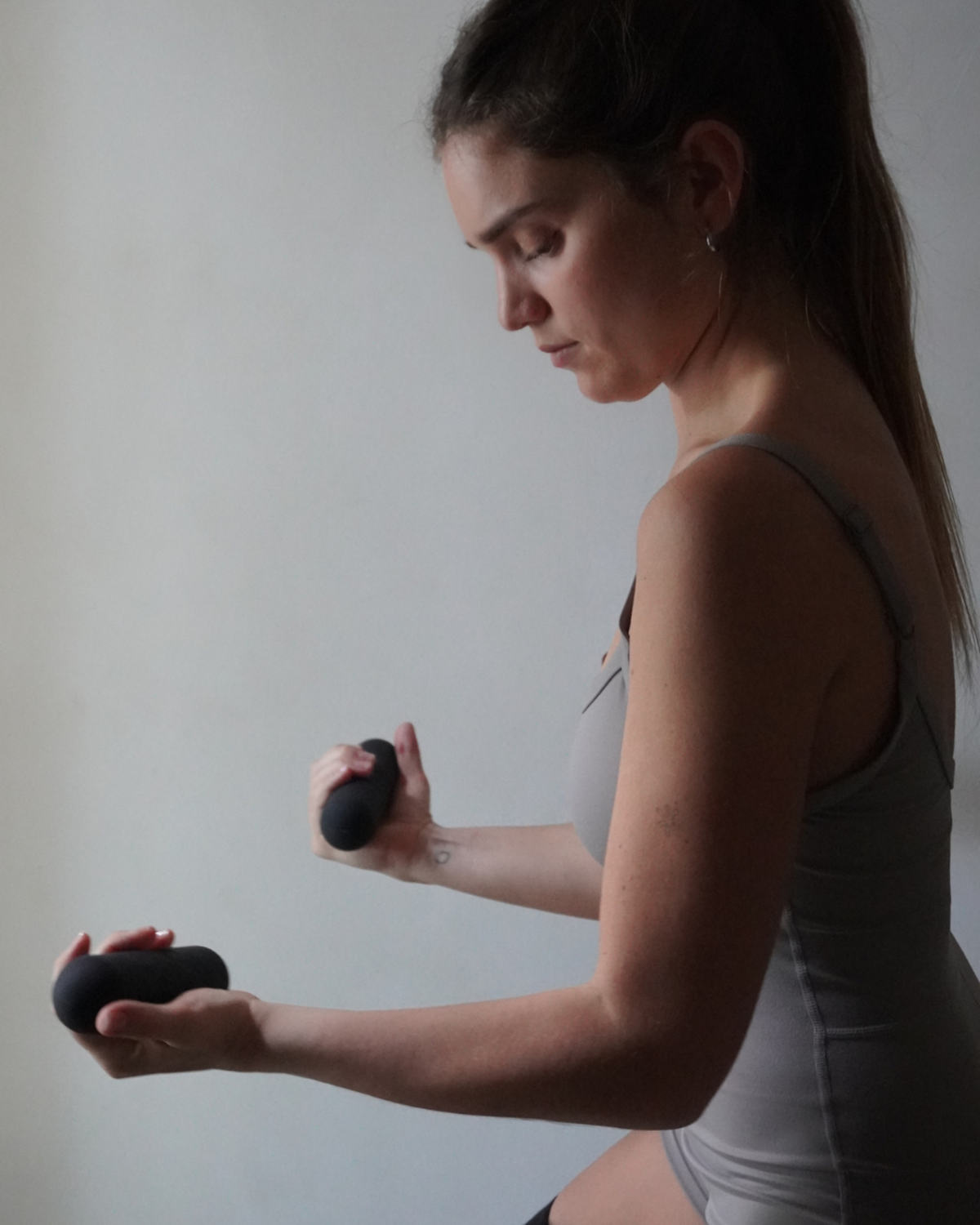 Woman exercising with black weights against a plain background