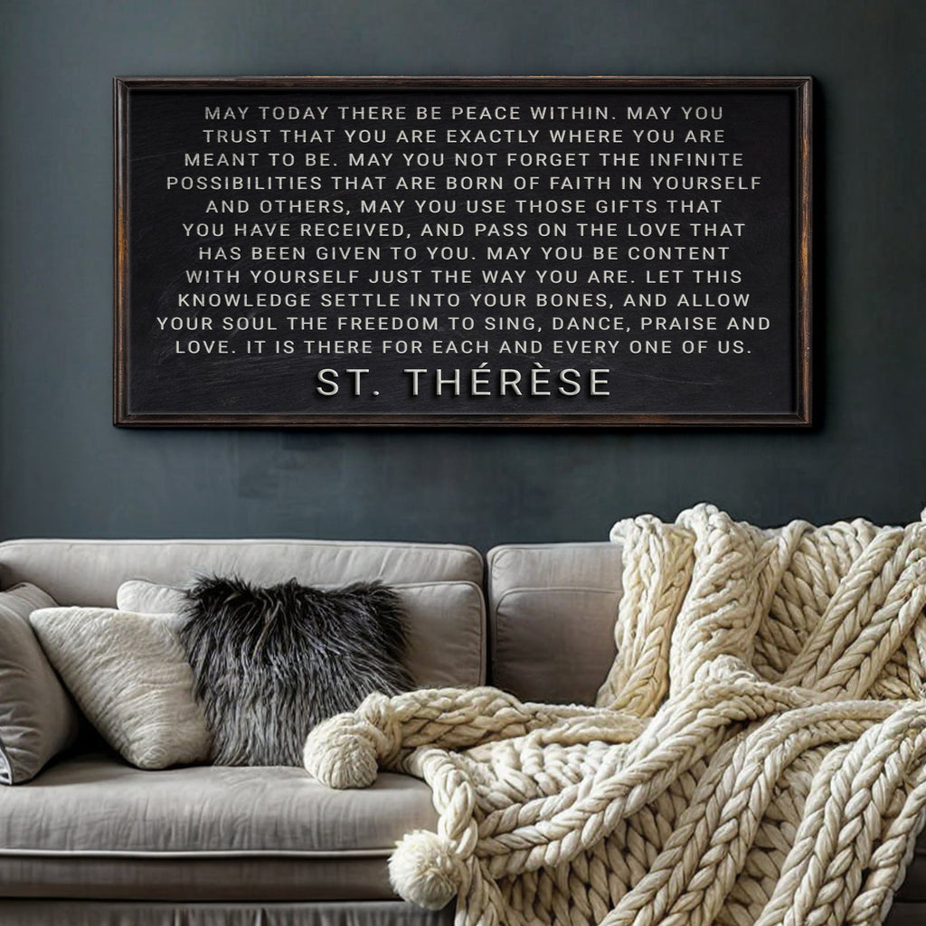 Framed St. Therese quote on a wall above a sofa with decorative pillows and a blanket.