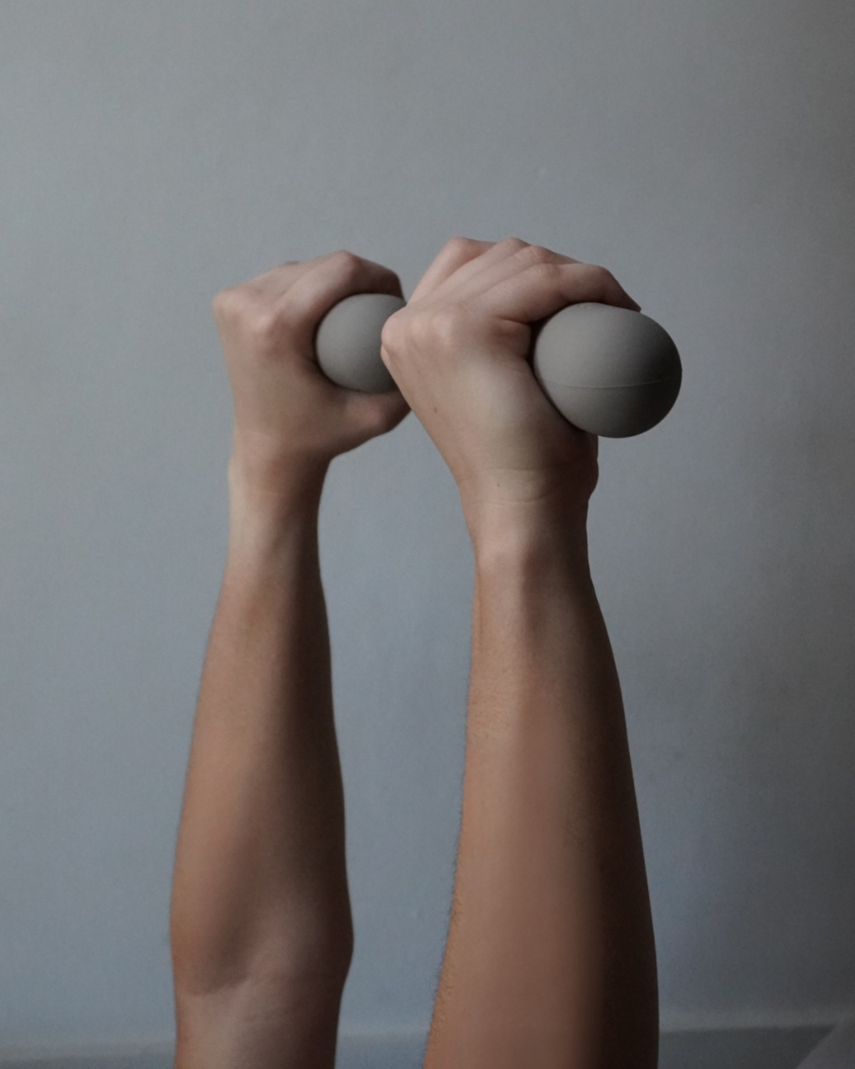 Two hands holding gray dumbbells against a plain background