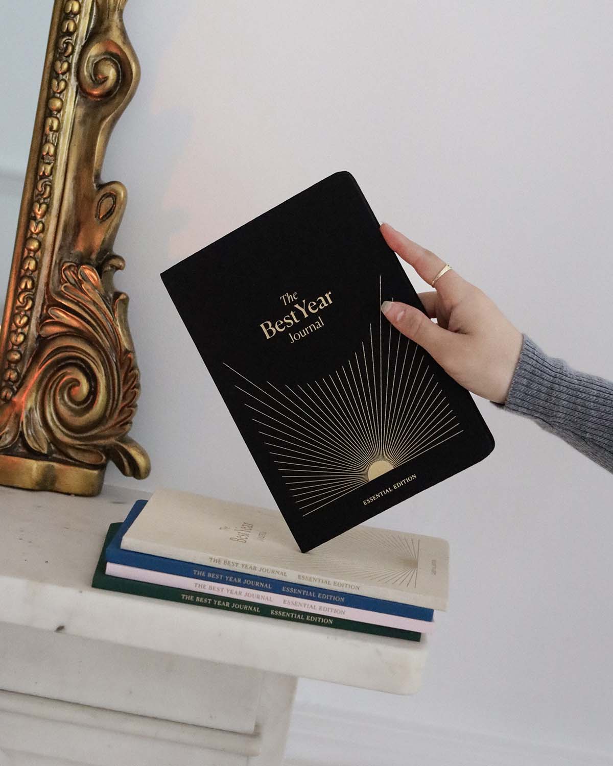 Person holding a black journal titled 'The Best Year Journal' on a white surface with decorative elements.