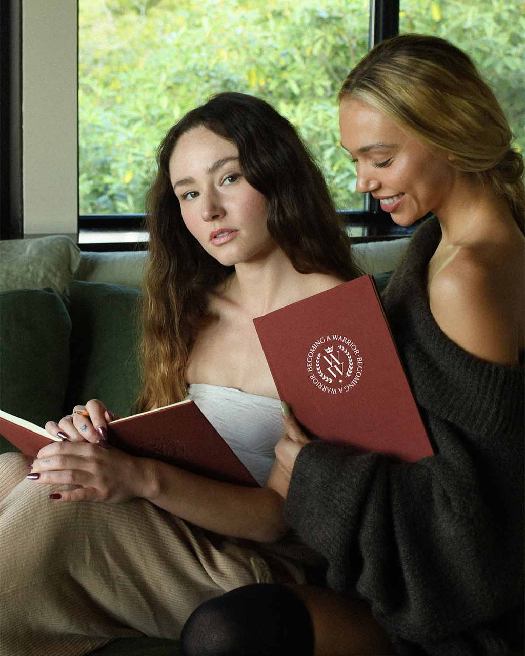 Two women sitting together, each holding a red book with a visible logo.