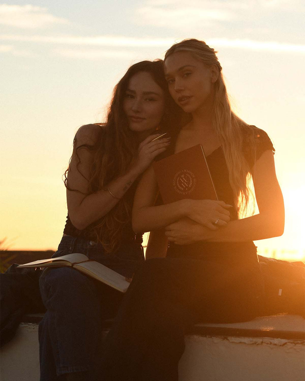Two women sitting together with books at sunset.