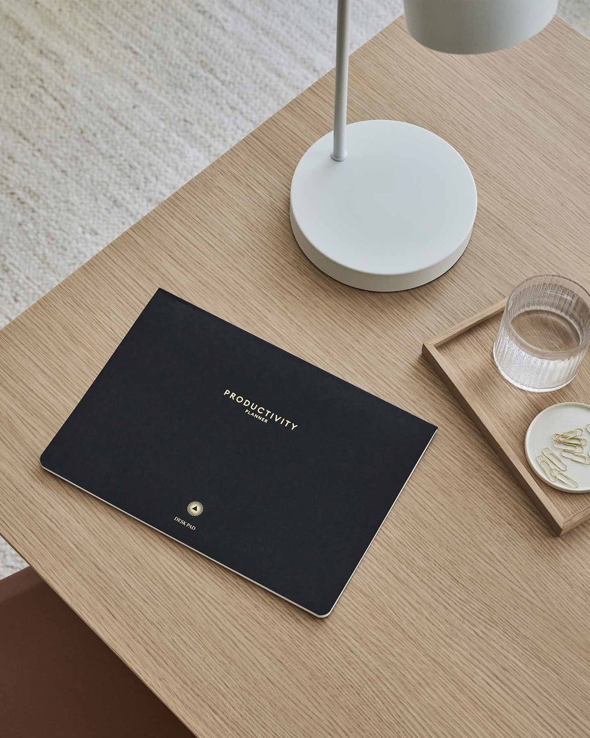 Black notebook titled 'Productivity' on a wooden table with a lamp and glass of water.