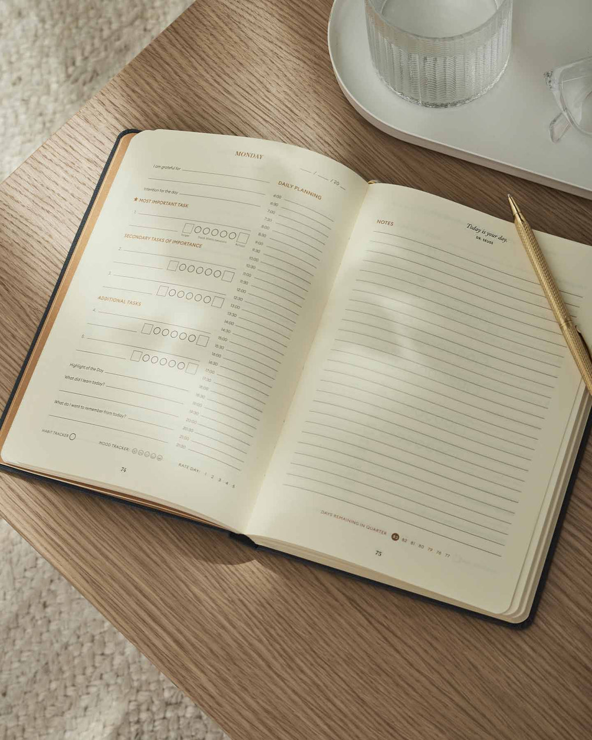 Open notebook on a wooden table with a pen and glass of water in the background