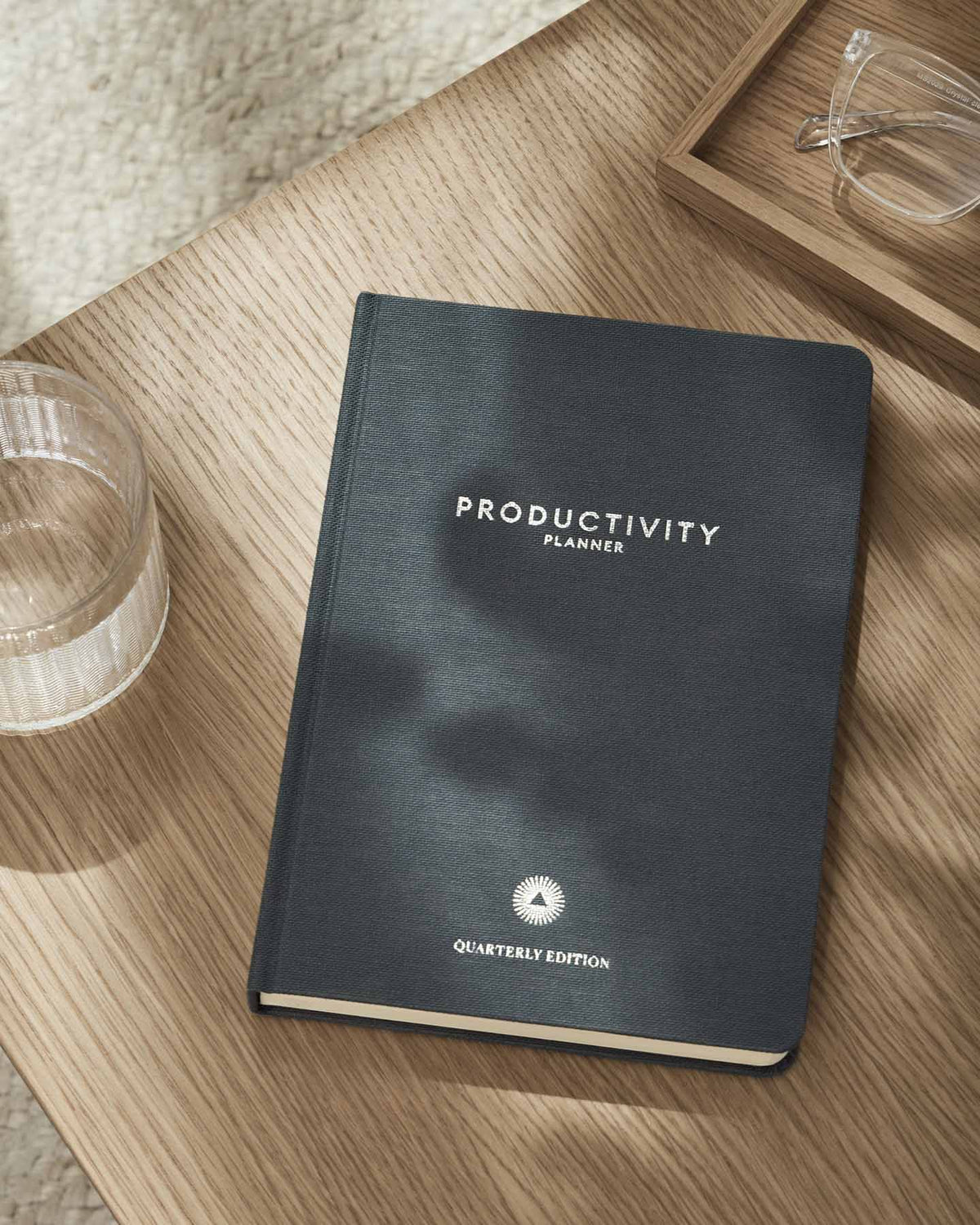 Productivity planner on a wooden surface with glasses and a glass of water.