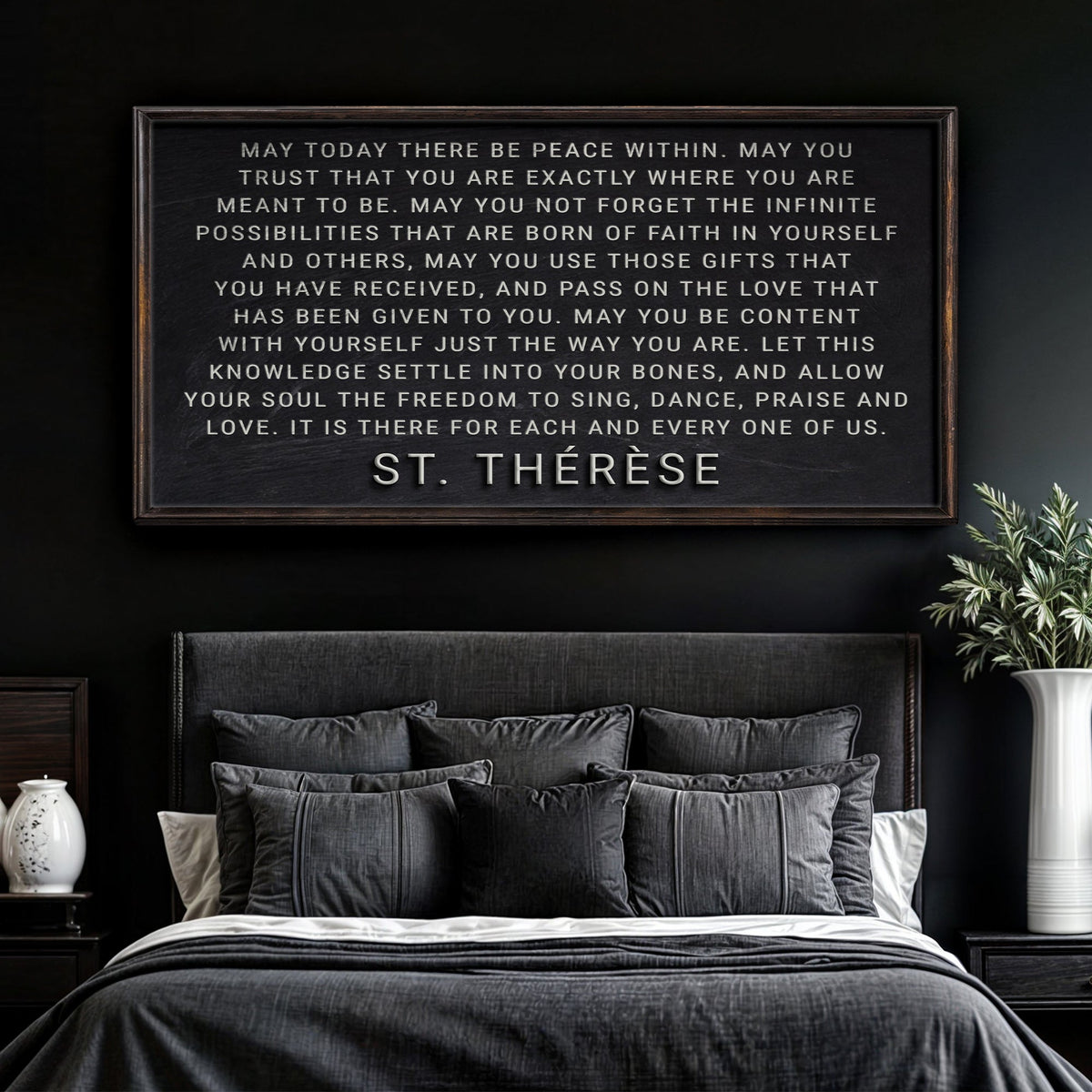 Bedroom with a framed quote on the wall, dark walls, and a bed with gray bedding.