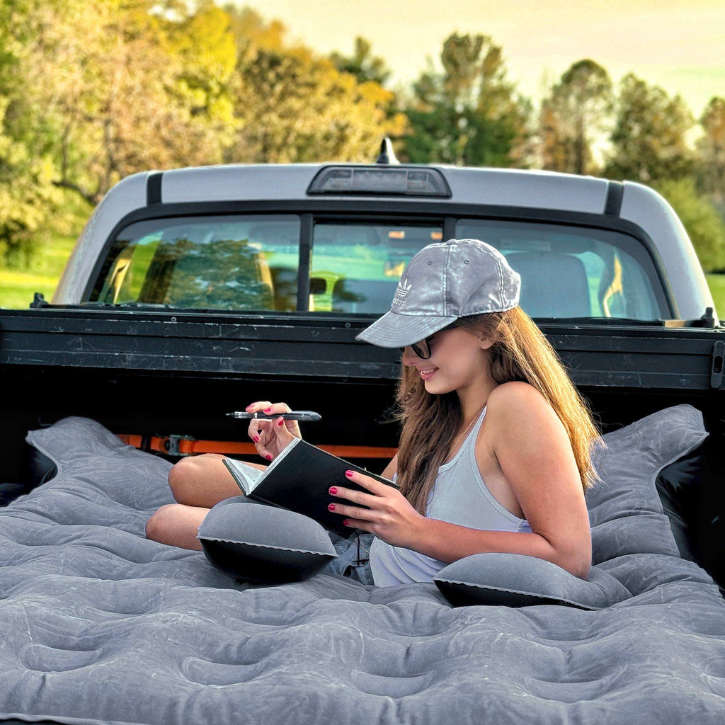 Woman sitting on an inflatable mattress in the back of a truck, writing in a notebook.