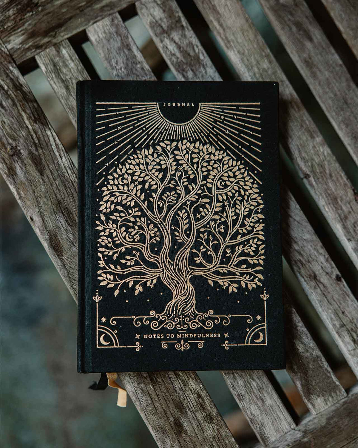 Black notebook with gold tree design on a wooden surface