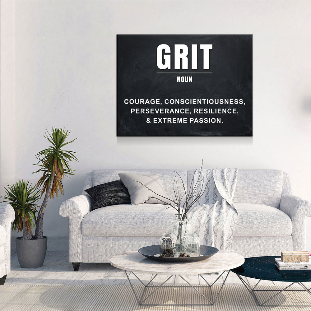 A black canvas wall art print featuring the word 'GRIT' and a dictionary-style definition, displayed above a light gray sofa in a modern living room setting.