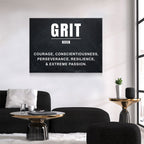 A black rectangular wall art print with the word 'GRIT' in large white letters and a dictionary-style definition below, displayed above a black sofa in a modern living room.