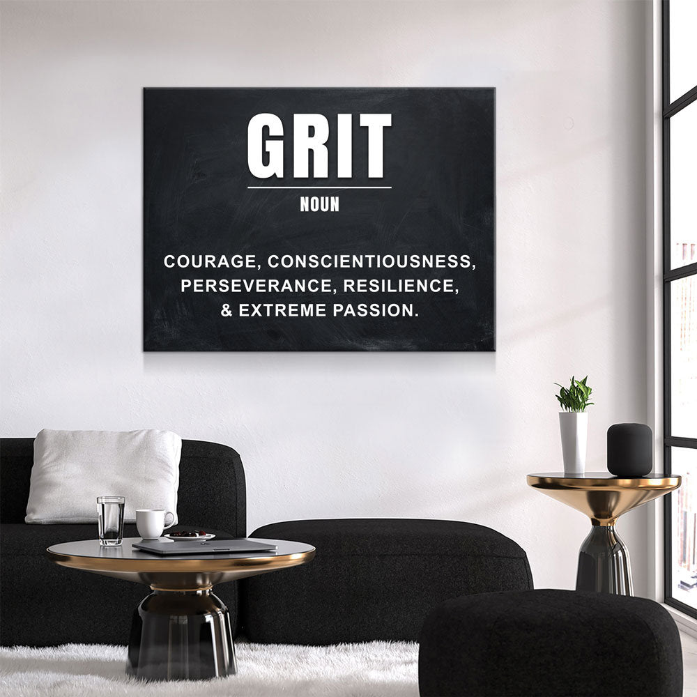 A black rectangular wall art print with the word 'GRIT' in large white letters and a dictionary-style definition below, displayed above a black sofa in a modern living room.