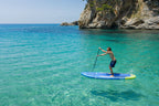 Person paddleboarding in clear blue water with rocky cliffs in the background