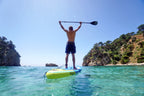 Person paddleboarding in clear blue water with rocky cliffs in the background