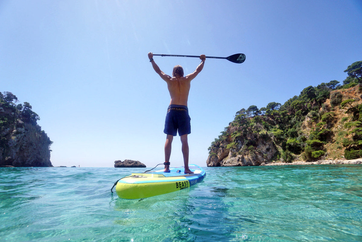 Person paddleboarding in clear blue water with rocky cliffs in the background