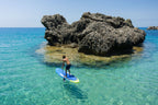 Person paddleboarding in clear blue water near a rocky island