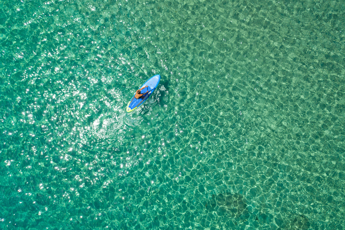 Person kayaking in clear turquoise water from an aerial perspective