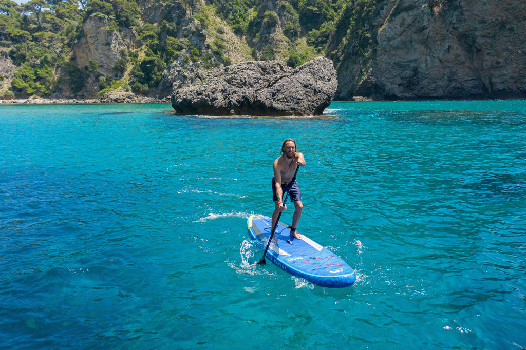 Person paddleboarding in clear blue water with rocky cliffs in the background