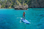 Person paddleboarding in clear blue water with rocky cliffs in the background
