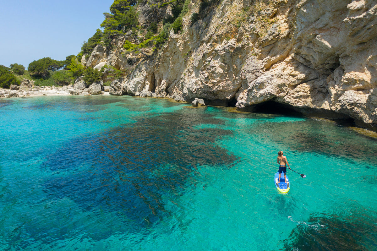 Person paddleboarding in clear blue water near a rocky coastline