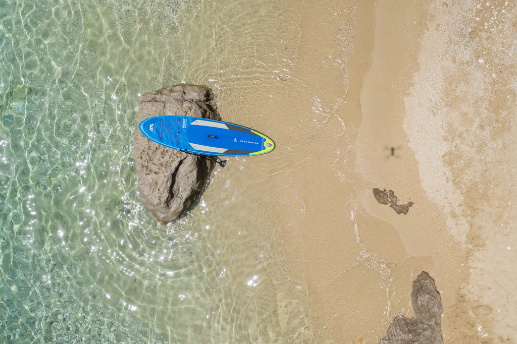 Blue paddleboard on a sandy beach with clear water
