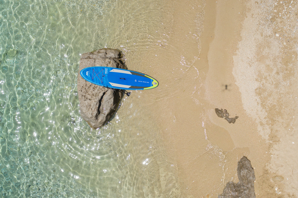 Blue paddleboard on a sandy beach with clear water