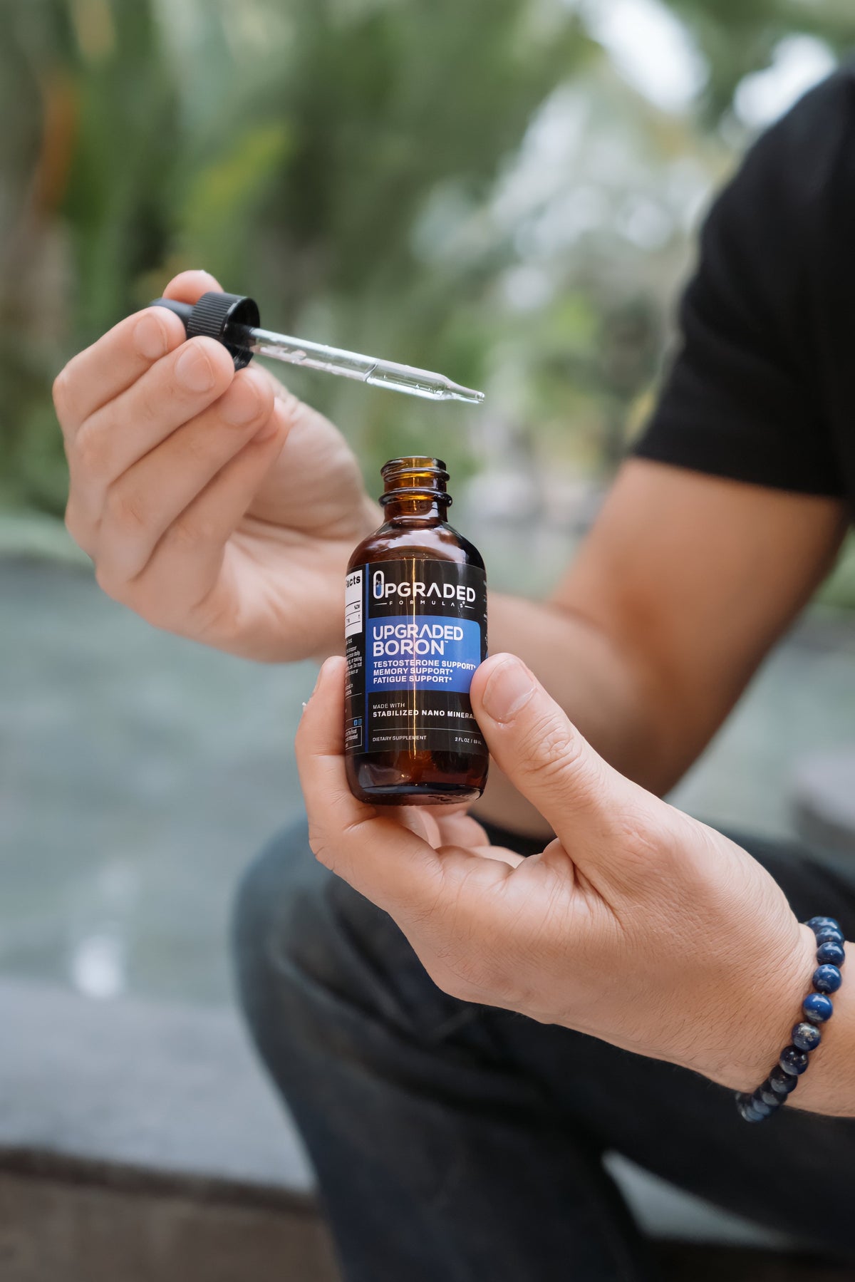 Person holding a bottle of 'Upgraded Boron' supplement with a dropper.