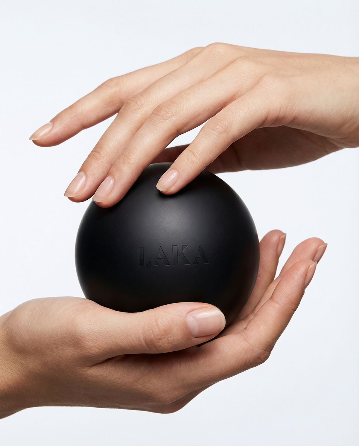 Black stress ball with 'LAKA' branding held by two hands on a light gray background