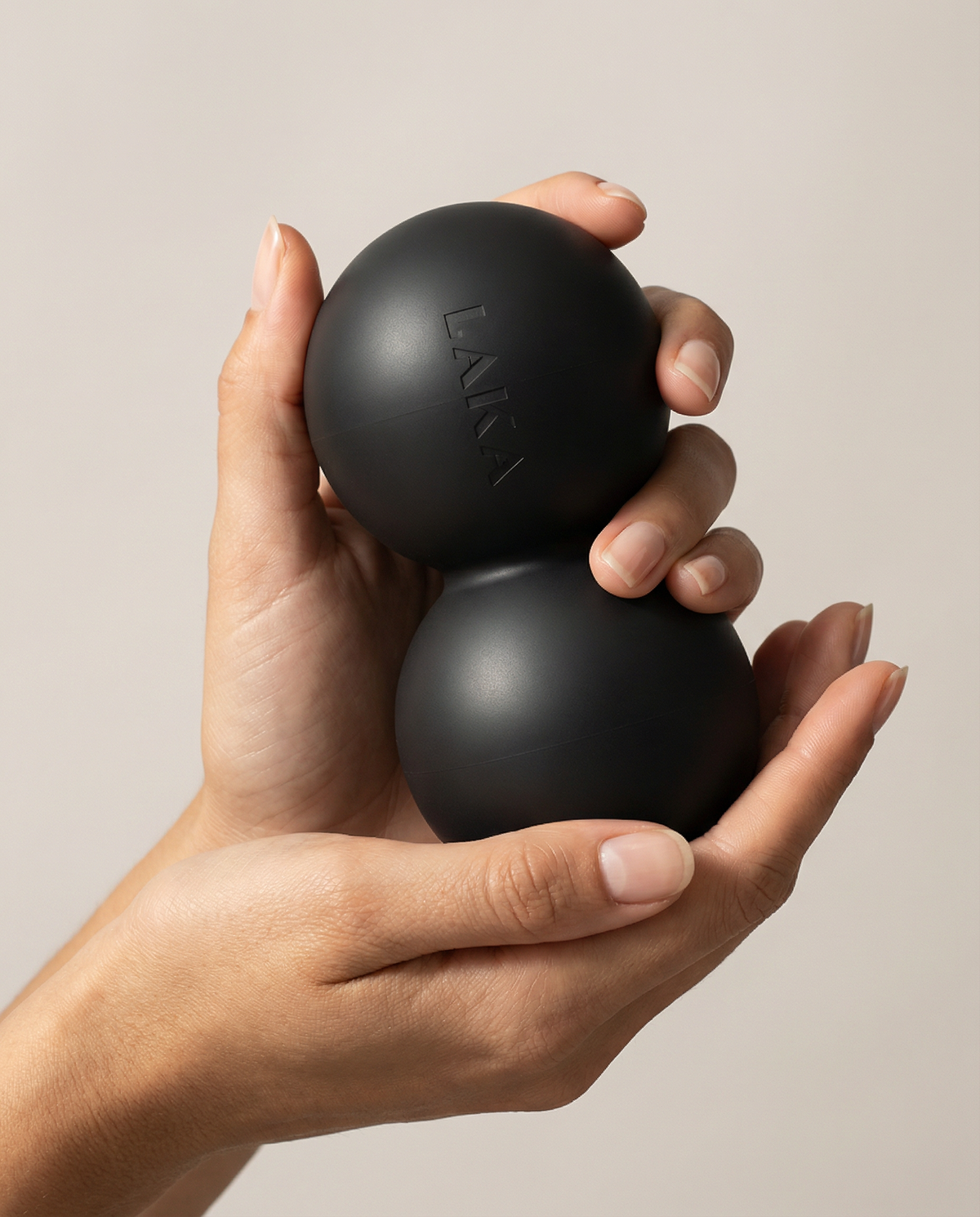 Two black massage balls held in a hand against a beige background