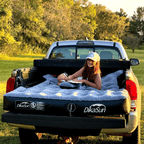 Person sitting on a DikaSun air mattress in the back of a pickup truck outdoors.