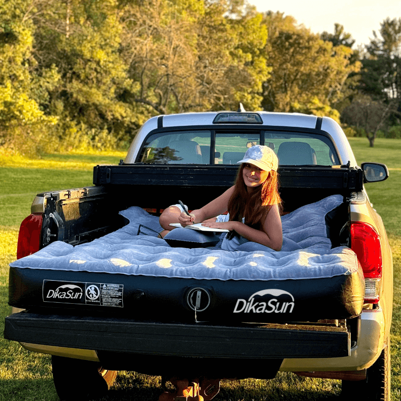 Person sitting on a DikaSun air mattress in the back of a pickup truck outdoors.