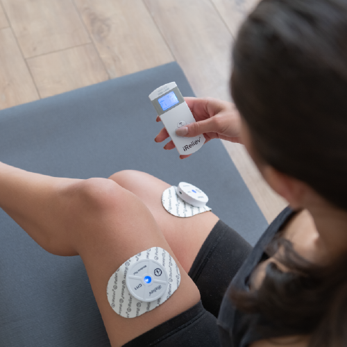 Person using a digital device on their knee with patches, possibly for medical or therapeutic purposes.