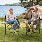 Two people sitting in camping chairs by a lake with a tent in the background