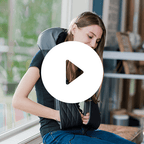 Woman using a black neck and shoulder massager in a home setting.