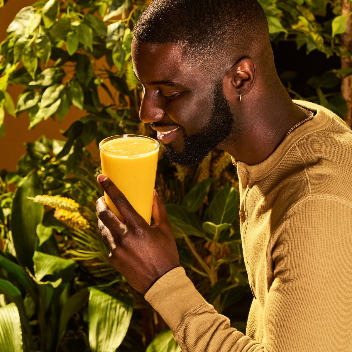 Man holding a glass of orange juice surrounded by green plants