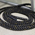 Coiled black battle rope with yellow accents on a concrete surface