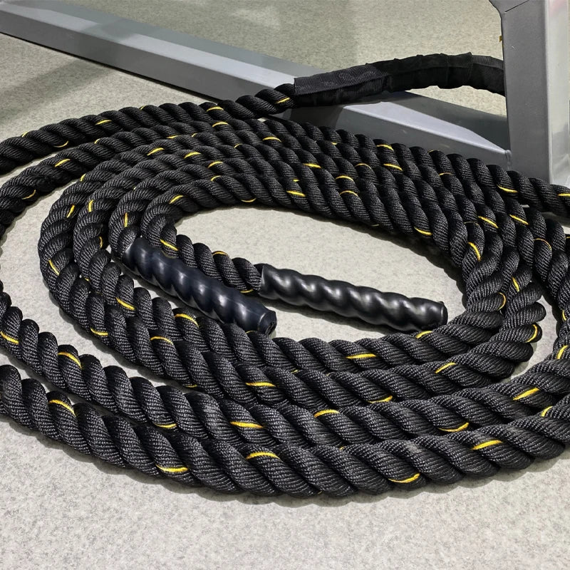 Coiled black battle rope with yellow accents on a concrete surface