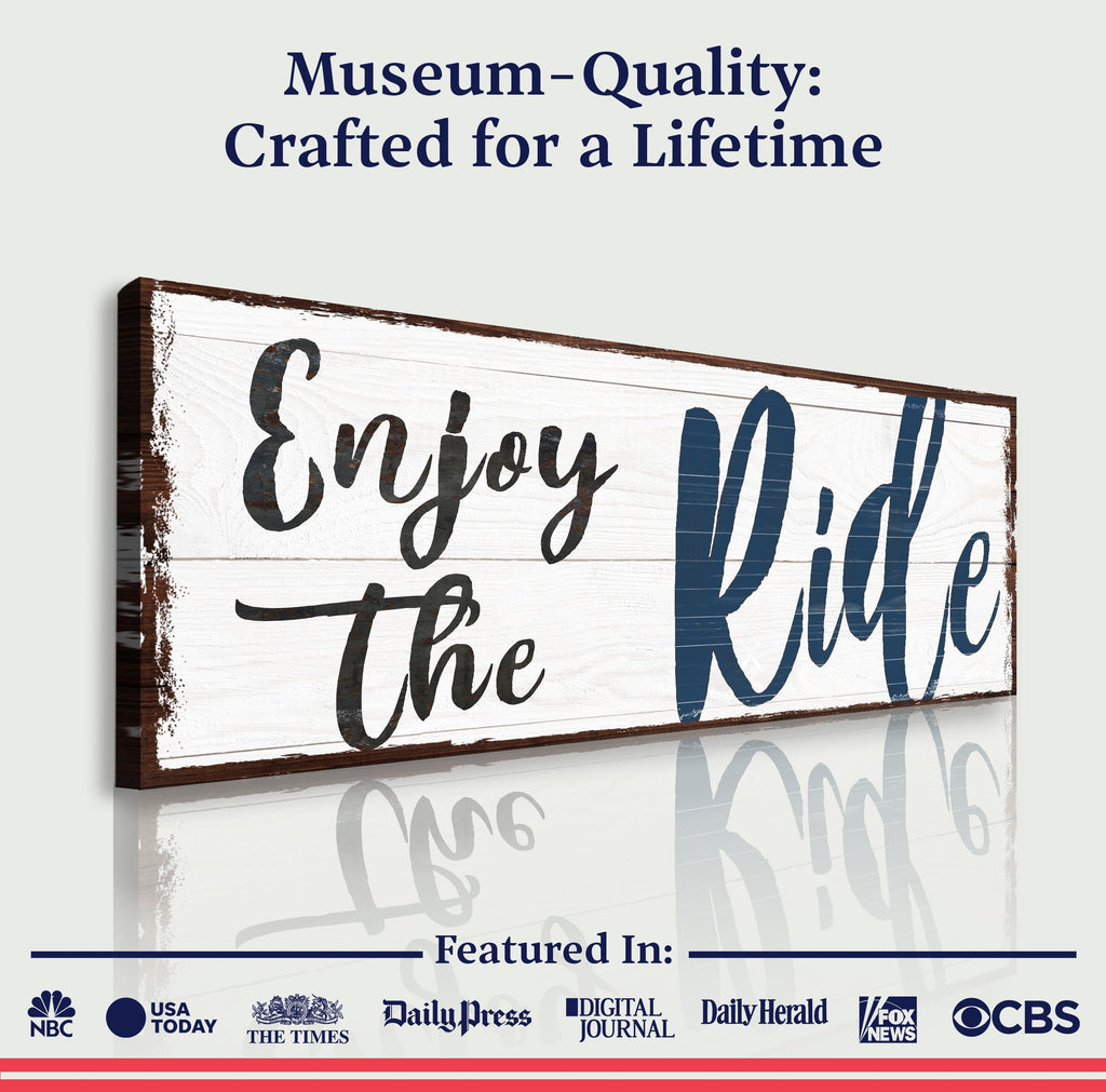Wooden sign with 'Enjoy the Ride' text on a white background, featuring media outlet logos at the bottom.