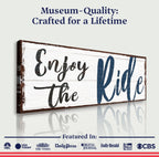 Wooden sign with 'Enjoy the Ride' text on a white background, featuring media outlet logos at the bottom.