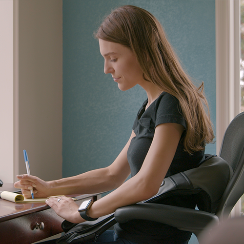 Woman sitting at a desk with a pen and paper, wearing a black shirt.