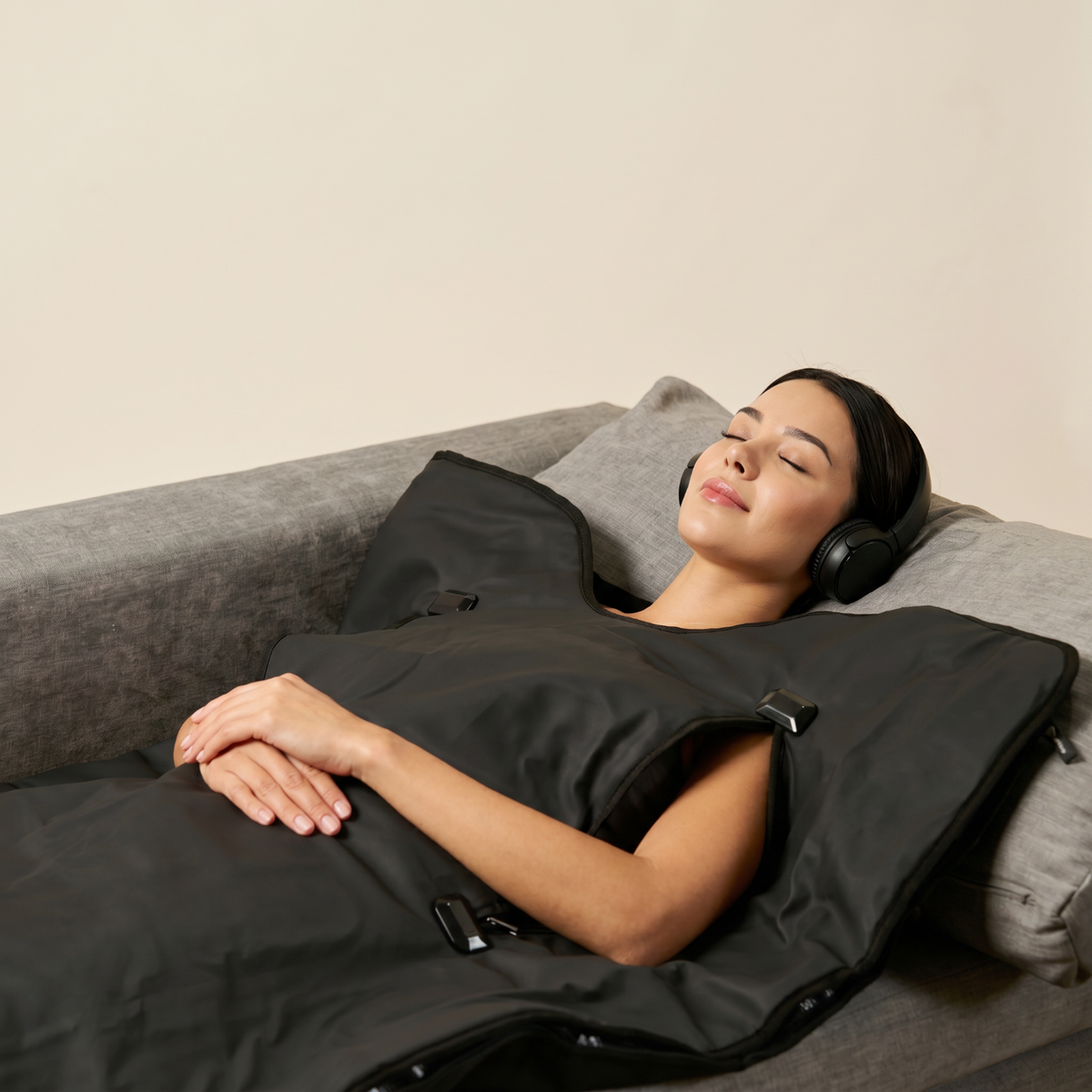 Woman lying on a couch with a black hooded blanket and headphones, possibly in a spa or relaxation setting.