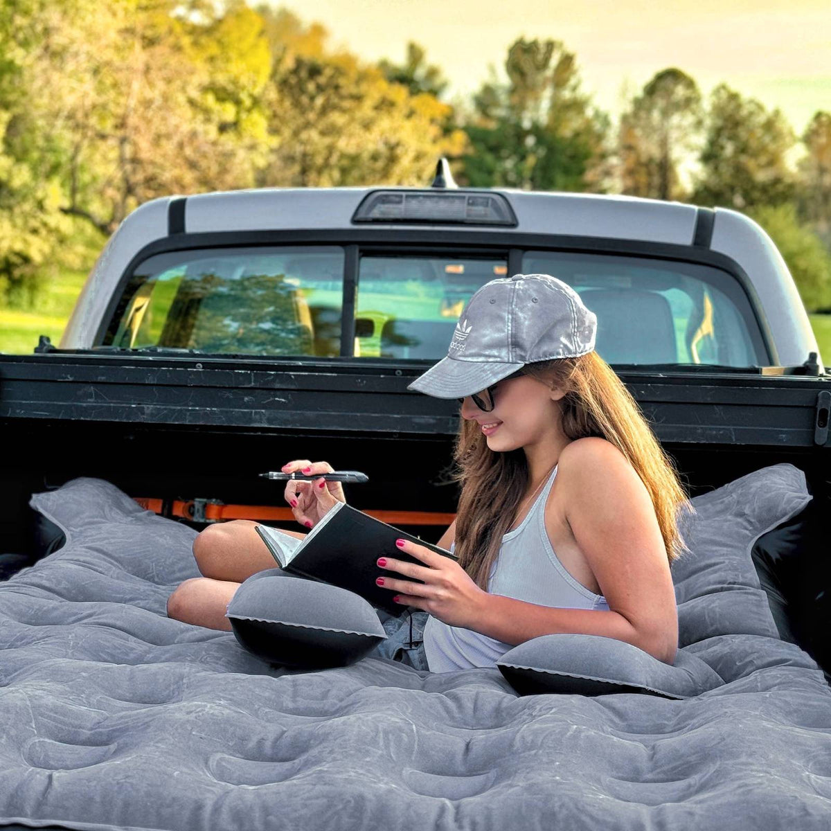 Woman sitting on an inflatable mattress in the back of a truck, writing in a notebook.