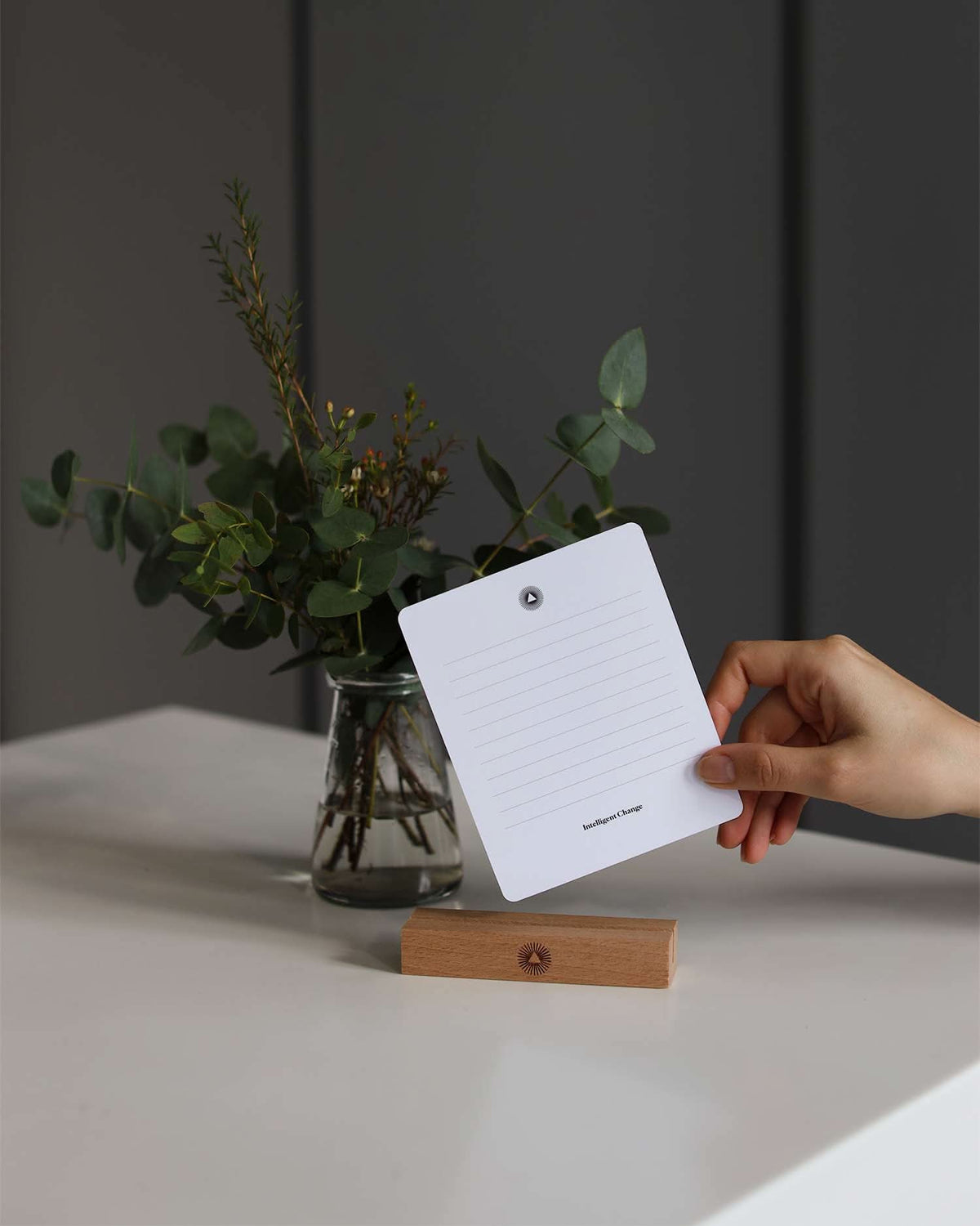 Hand holding a color swatch card with a vase of greenery in the background