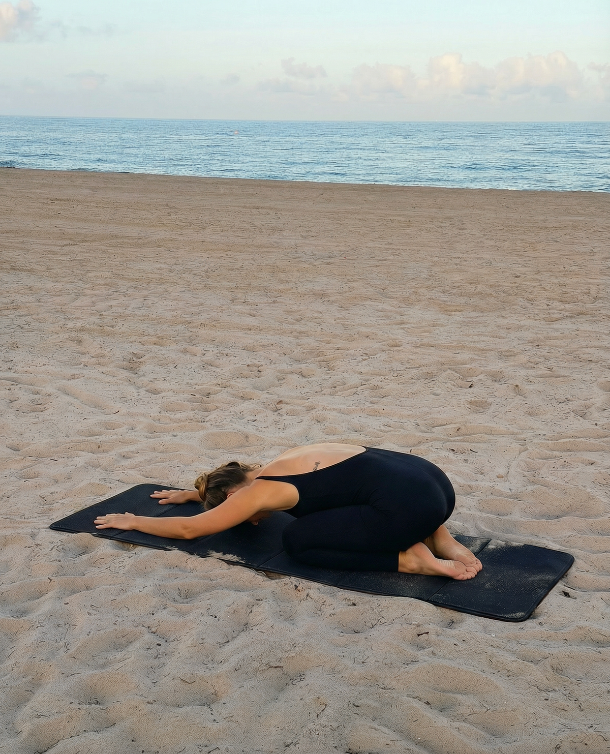 Person practicing yoga on a beach with ocean in the background